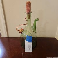 Full view of green glass decanter showing side spout and stopper with fiber tassel