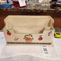 Front view showing two-compartment wooden organizer with fruit motif and checker border