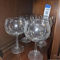 Six clear balloon wine glasses on shelf, front view showing bowl shape and stems