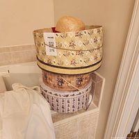 Two patterned cylindrical hat boxes stacked; top box open showing straw hat