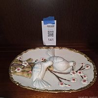 Front view of oval plaster plaque showing two doves on flowering branch with gold border