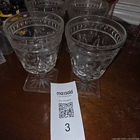 Four clear pressed glass goblets on wooden surface