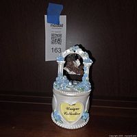Front view of assembled trinket box showing brand plaque, floral details, and hanging cherub