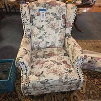 Front view of floral wingback armchair showing upholstery, nailhead trim, removable cushion, wooden legs