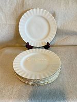 Stack of eight white fluted plates with gold trim, one standing upright