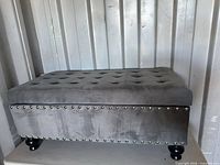 Front view of gray tufted velvet storage ottoman showing nailhead trim and legs