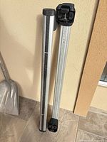 Two aluminum cross bars with black end caps leaned against wall