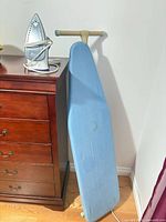 Steam iron atop dresser with ironing board leaning against wall