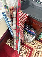 Wrapping paper rolls leaning against furniture beside tote of gift bags