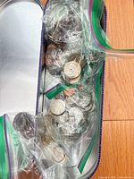 Open metal tin showing zip bags containing mixed international coins
