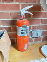 Full view of orange fire extinguisher standing on workbench