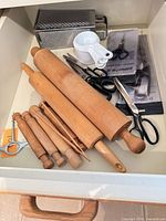 Drawer view showing rolling pins, grater, measuring cups, scissors, pegs, corkscrew