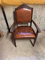Front view of wooden armchair with brown leather upholstery and nailhead trim
