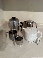 Group shot of electric kettle, two stovetop coffee pots and two milk pitchers