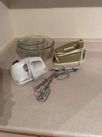 Green mixer, white mixer, clear bowls, beaters on countertop