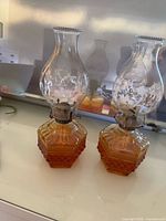 Front view pair amber glass oil lamps with patterned bases and decorated chimneys
