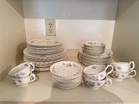 Stacks of dinner plates, salad plates, saucers, and four nested teacups showing floral pattern and gold trim