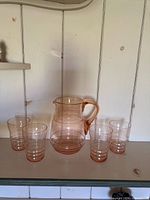 Rose coloured glass pitcher centered, flanked by four matching tumblers