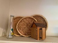 Woven bamboo trays, glass bottle, wooden birdhouse key holder on shelf