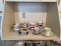 Shelf showing multiple stacks of assorted floral china teacups and saucers
