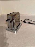 Front angled view showing chrome body, diamond pattern, black knobs, attached cord