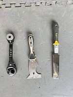 Three hand tools laid out: ratcheting wrench, paint scraper, FatMax pull saw