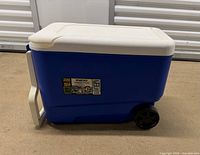 Side view of blue Igloo cooler showing wheels, lid, capacity label