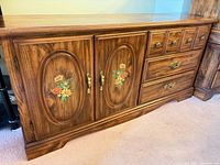 Front view of brown wood dresser showing drawers, cabinet doors with floral panels