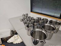 Wide view showing entire assortment of stainless steel buckets, pitchers, creamers and teapots on table