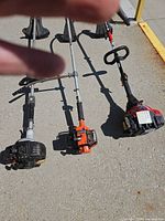 Three gas string trimmers laid out showing entire length, engines and cutting heads
