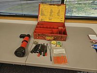 Tool, driver bars, fasteners, load tins and open metal case displayed on table