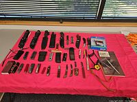 Overview of entire lot on table: fixed blades, folding knives, multitools, sheaths, booklet and boxes