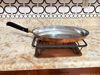 Oval copper skillet resting on black metal stand over copper tray