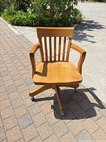 Front view of oak swivel office chair showing seat, arms, casters