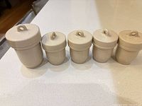 front view of five cream ceramic egg coddlers showing sizes and lids