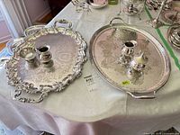 Two silver-plate handled trays with sugar bowls and creamers displayed on table