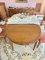 Full view of oval wood dining table with pads folded on top, chairs visible but not included