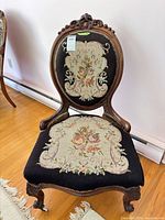 Front view of Victorian needlepoint parlor chair showing carved crest, floral tapestry upholstery, cabriole legs with casters