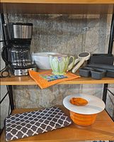 Shelf with coffee maker, bowl, pitcher, utensil, loaf pan tray; lower shelf with hot pad and salad spinner