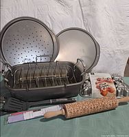 Group shot of all items: roasting pan with rack, two pizza pans, boxed gingerbread cake pan, decorative rolling pin, dough guide set