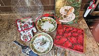 Overview showing all items: glass platter, two ceramic plates, cookie cutters, mitt/pot holder, pie server, metal crackers and Santa figurines