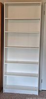 Front view of tall white shelving unit showing all six shelves