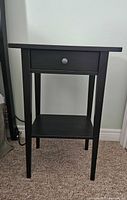 Front view of black wood night table showing drawer and shelf