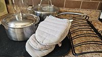 Overall view: two stainless pots with lids, black roasting rack, grey oven mitts
