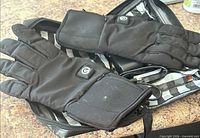 Pair of black heated gloves lying in open striped-lining zip bag, showing power button and battery pocket