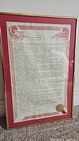 Full view of framed document showing gold frame, red mat, entire printed text and seal