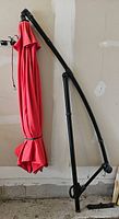 full view of folded red umbrella on black curved support pole leaning against wall