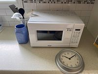 Microwave with jar, utensils, clock visible