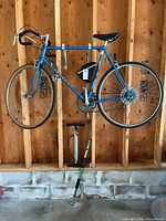 Full view of blue Peugeot road bike hanging, with pump and chin-up bar below