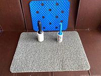 Overall lot: two lint rollers on grey litter mat with blue perforated mat behind